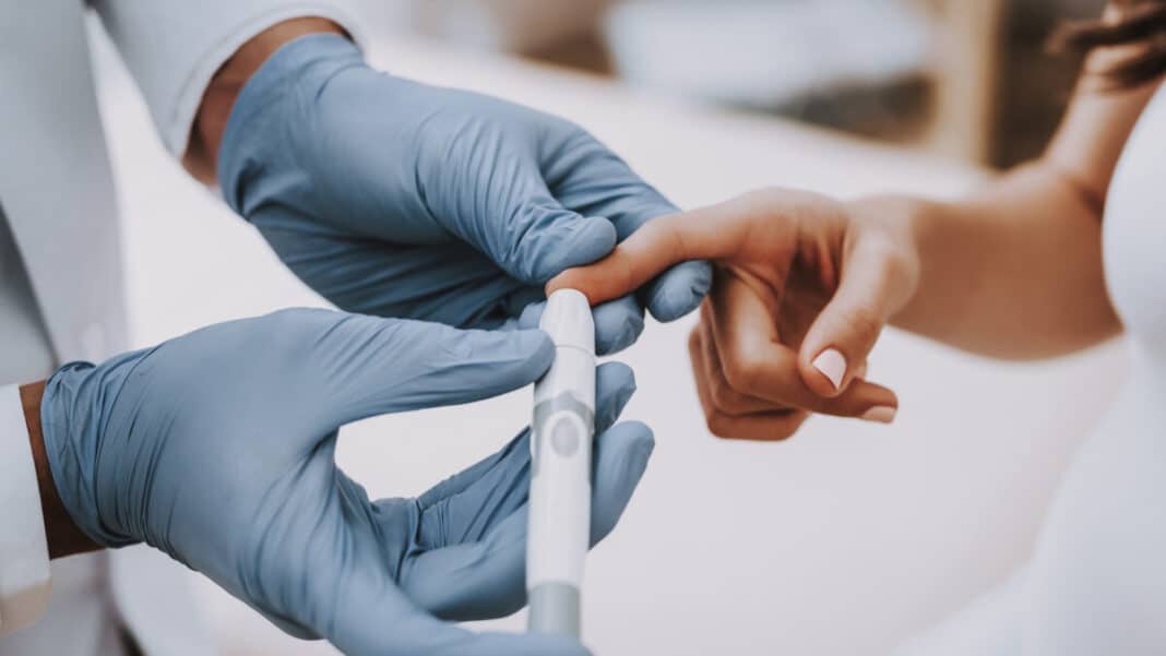 Personnel médical avec des gants qui prend la mesure de la glycémie dans le sang à une personne sur l'un de ses doigts.