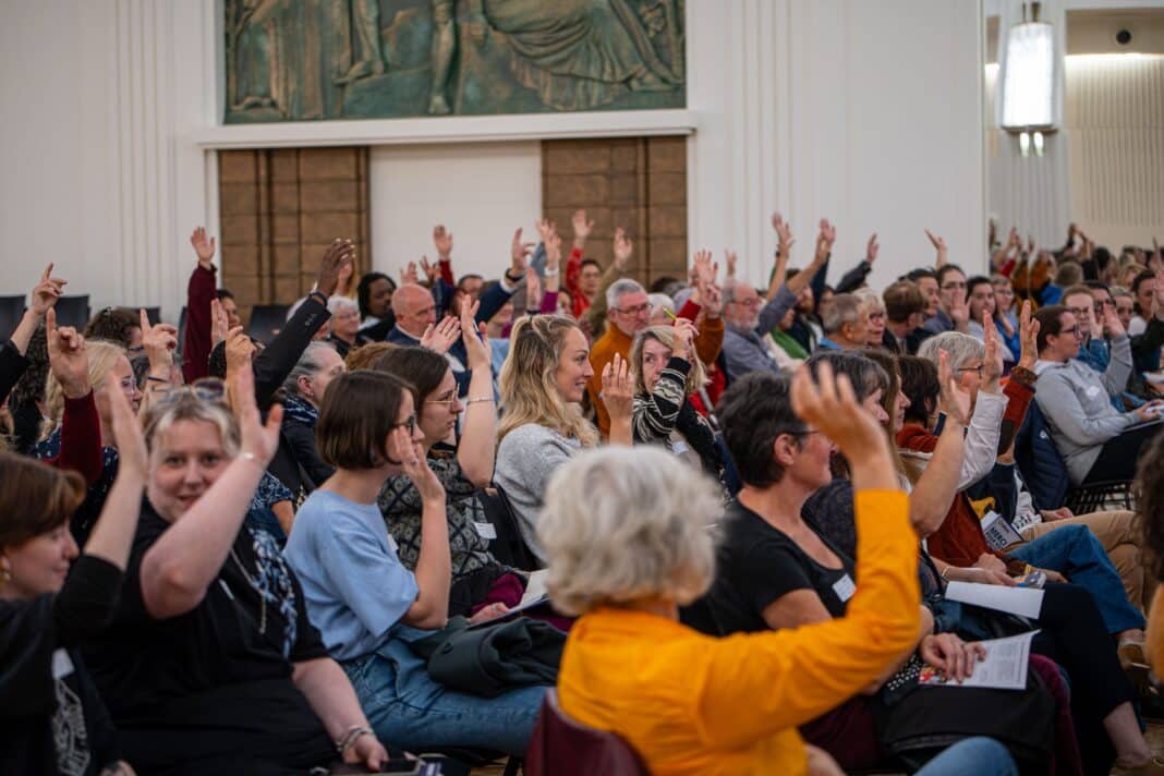 Des personnes assises dans une salle la main levée.