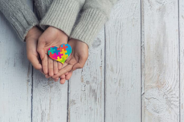 Un coeur en puzzle multicolore dans la main de deux enfants.