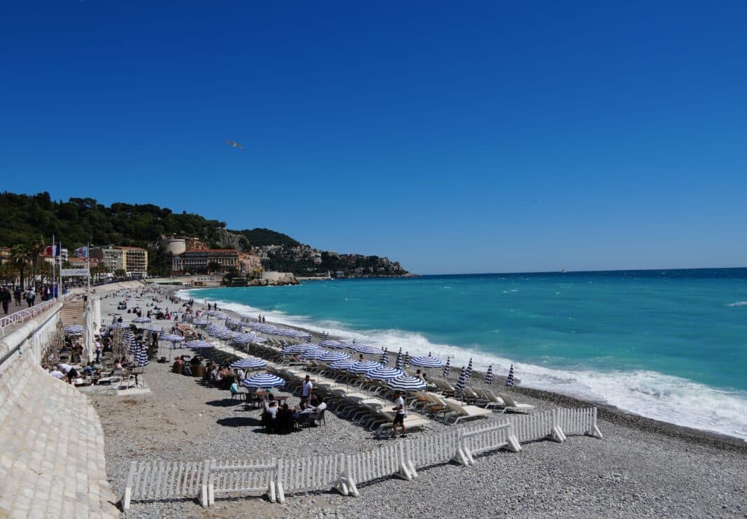 La promenade des Anglais sous le soleil avec un restaurant de plage ouvert et des clients en terrasse.