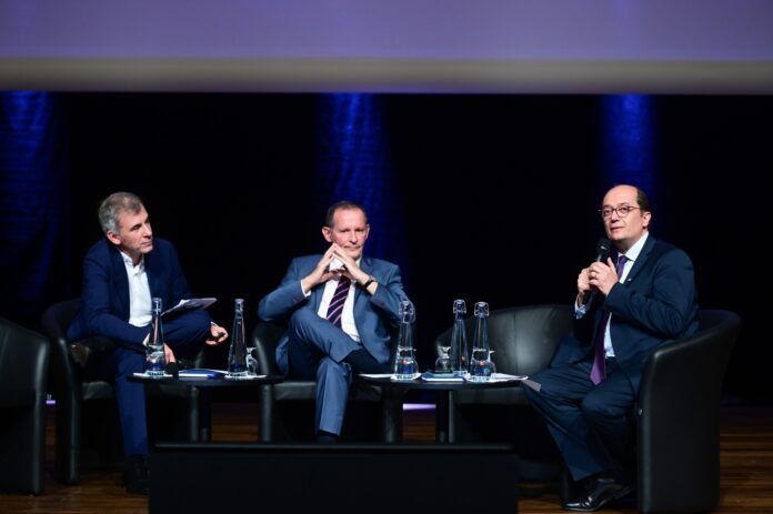 Gérard Bekerman au centre assis dans un fauteuil à l'occasion d'une conférence.