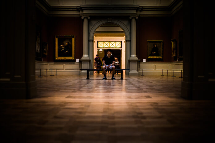 Un homme sur un banc dans une galerie en train de regarder des tableaux