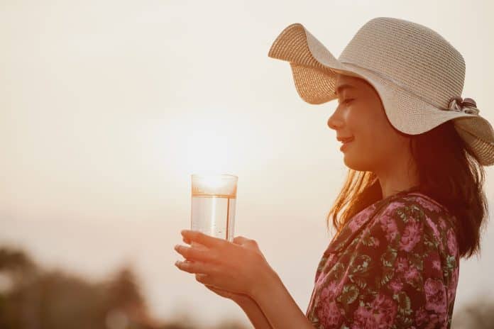 Canicule Une fille qui porte une robe a fleurs et un chapeau tenant un verre d'eau