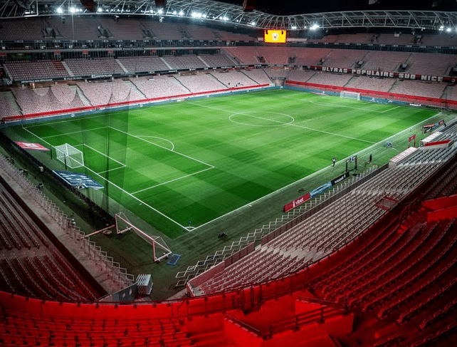 Le stade Allianz Riviera vue de l'intérieur avec des lumières rouges dans les tribunes et la pelouse éclairée.