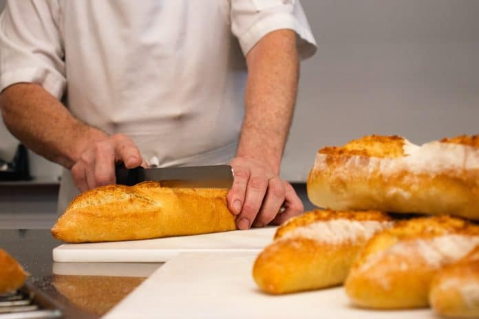 Un boulanger qui coupe une baguette de pain.