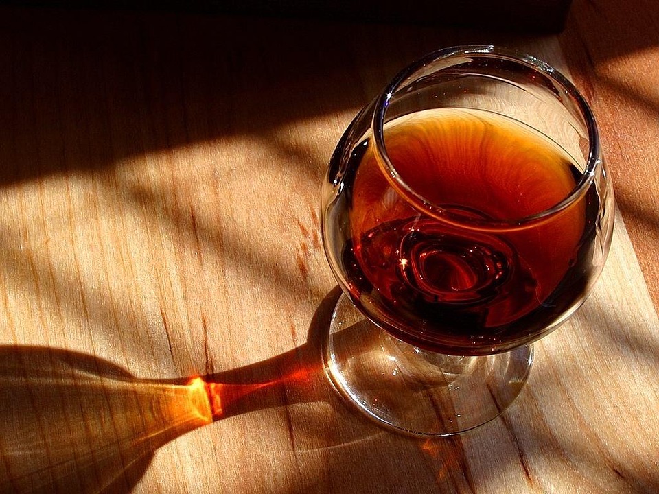 Un verre de cognac aux couleurs boisées avec un reflet sur une table.