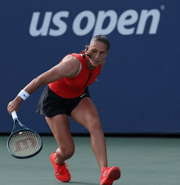 La joueuse de tennis Niçoise en tenue rouge et noir sur un court de l'US Open effectuant un revers.