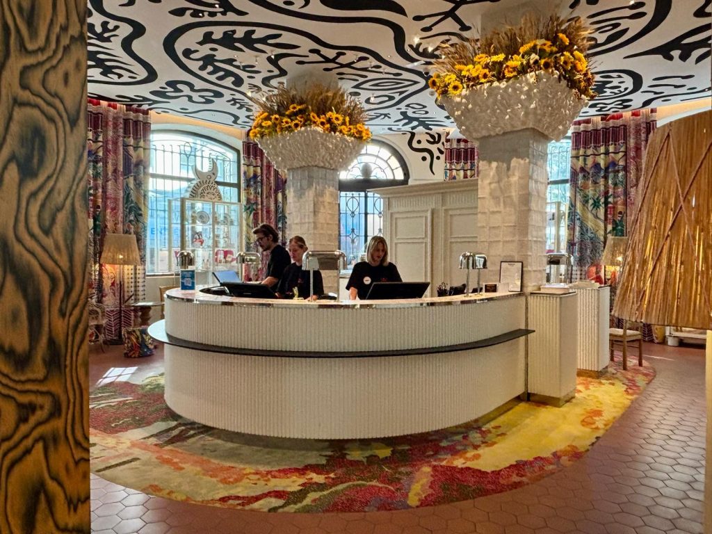 L'intérieur de l'hôtel Mama Shelter avec le comptoir d'accueil blanc dans une décoration très originale avec des fresques au plafond.
