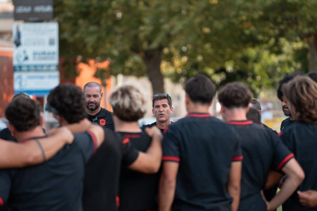 Les joueurs de Nissa Rugby en cercle entourant leur coach à l'entrainement habillé en noir.