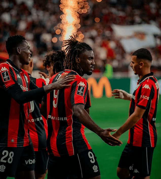 Les joueurs de l'OGC Nice se congratulent après la victoire contre Auxerre dans une ambiance festive avec des artifices en fond.