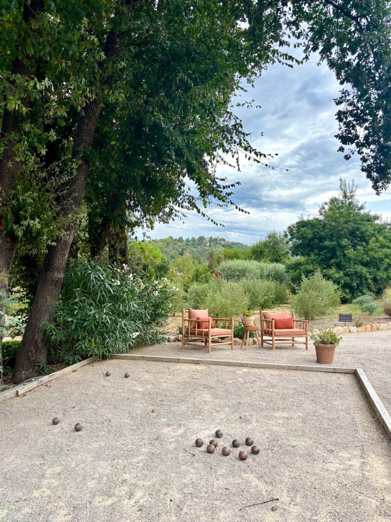 Le restaurant Toile Blanche et ses tables à l'extérieur dans un cadre champêtre très arboré et un terrain de pétanque.