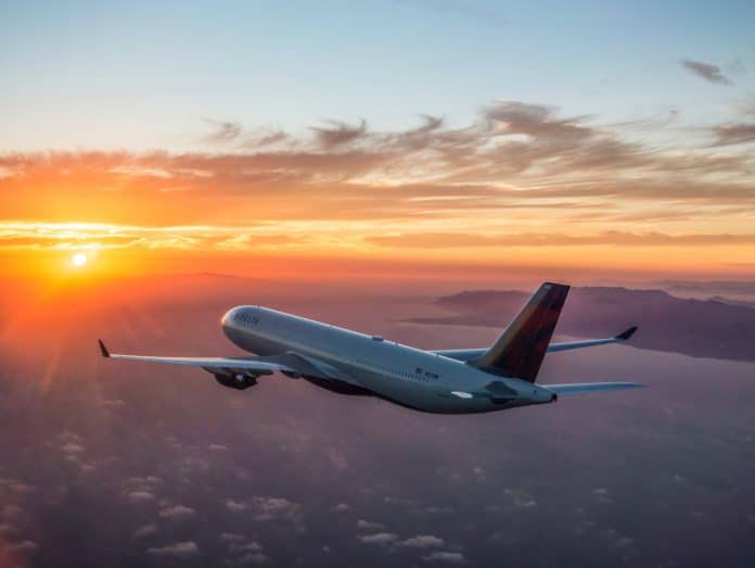 un avion de la compagnie Delta Air Line dans le ciel devant un couché de soleil.