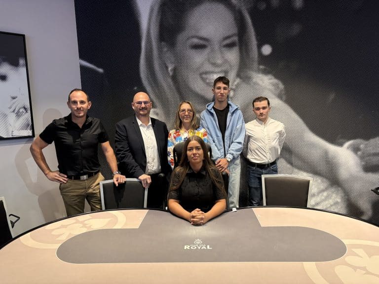 Plan large de la directrice de la formation, du responsable des jeux du casino ainsi que trois anciens élèves derrière une table de poker.