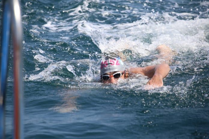 Un homme nage avec des lunettes et un bonnet de bain dans la mer.