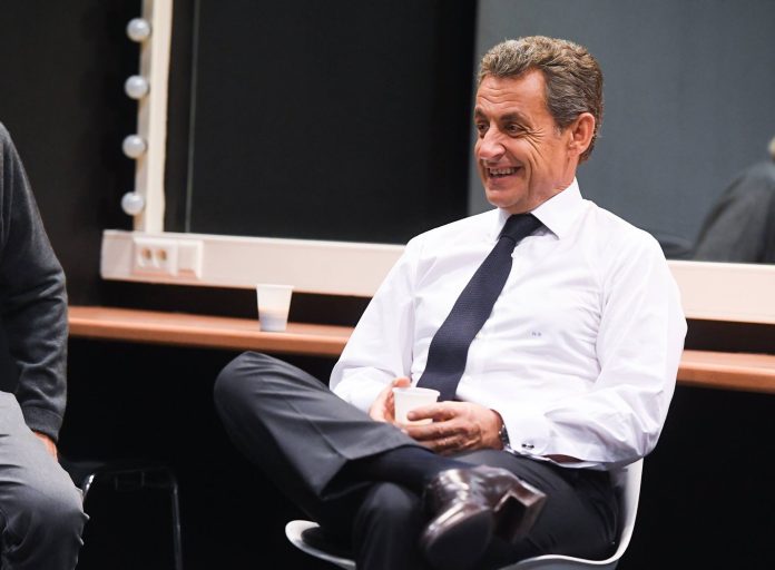 L'ancien président de la République Nicolas Sarkozy en chemise blanche cravate foncée assis sur une chaise