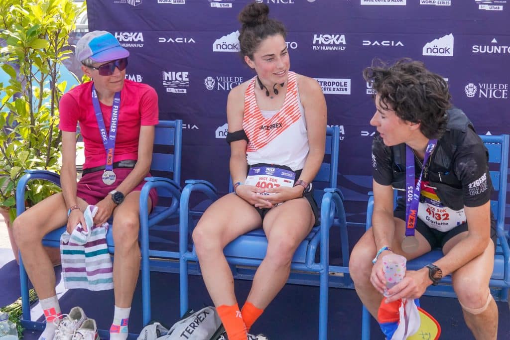 Un podium féminin avec leurs médailles en discussion sur des chaises bleus.