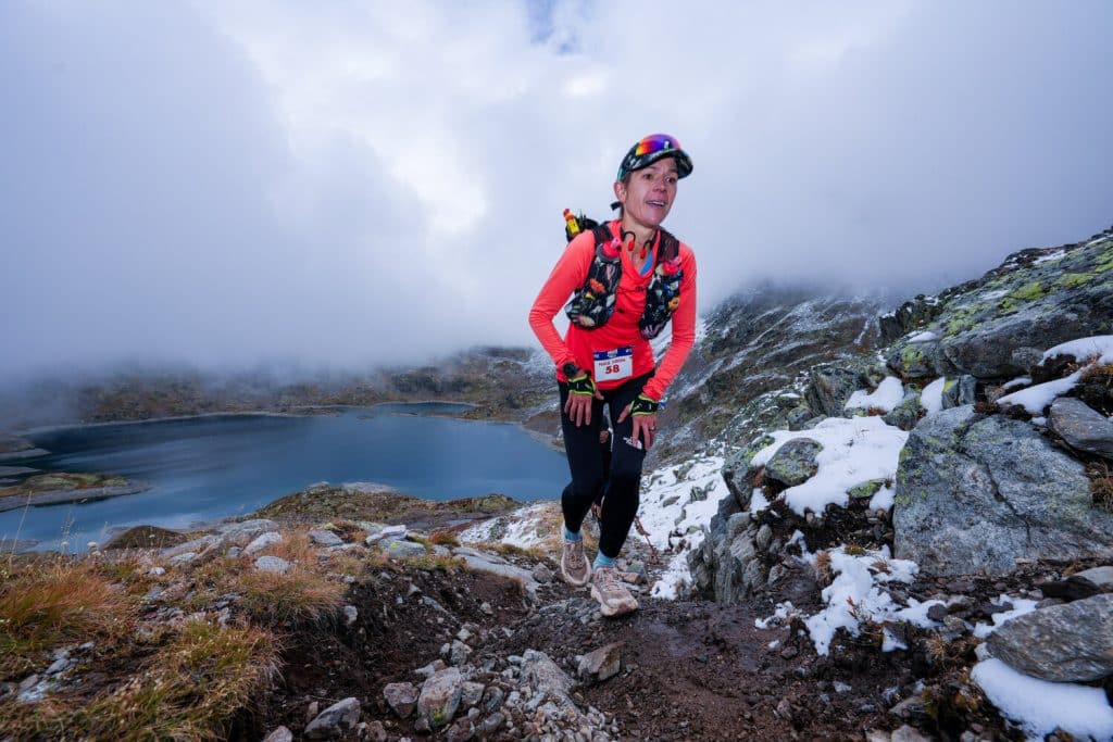 Une athlète bien couverte dans la montagne au bord d'un lac avec de la neige autour.