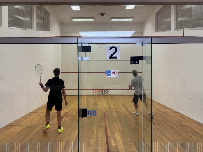 Terrain de squash à Vauban avec deux joueurs dans la cabine vitrée.
