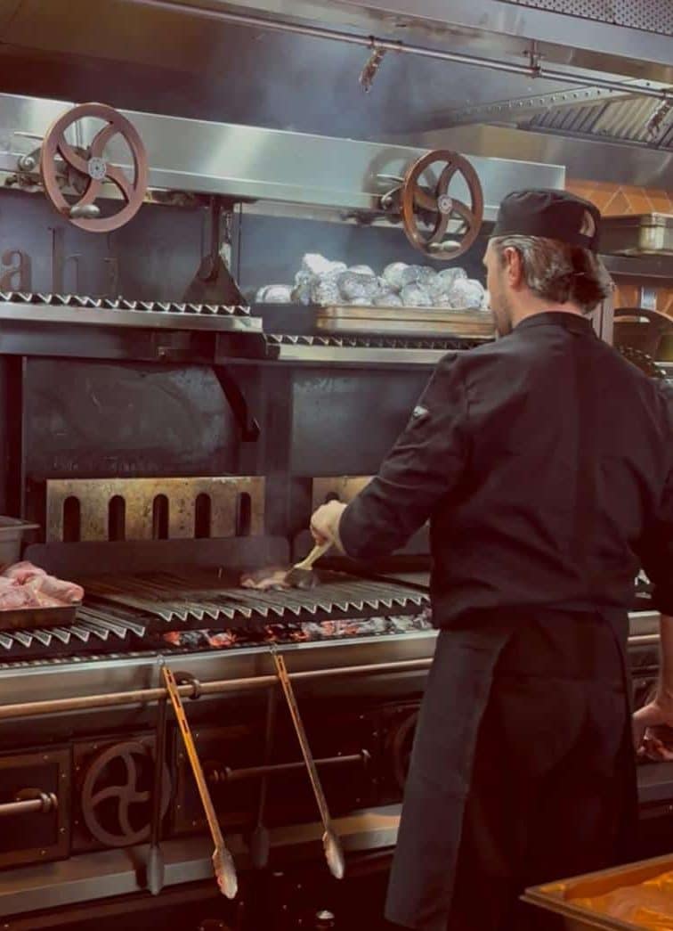Un des chefs aux fourneaux de dos devant un piano de cuisine.