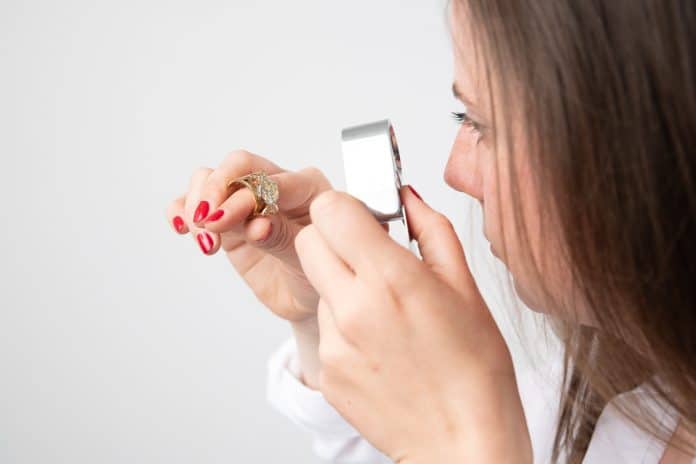 Une femme regarde à la loupe la valeur d'une bague dans sa main.