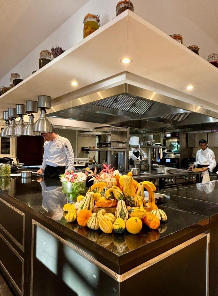 La cuisine du domaine avec le chef aux fourneaux et un grand tas de fruit sur le plan de travail.