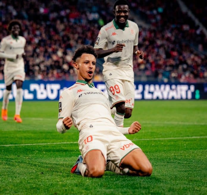 Le joueur de l'OGC Nice Sofiane Diop glisse sur la pelouse pour célébrer son but. Il joue avec un maillot blanc.