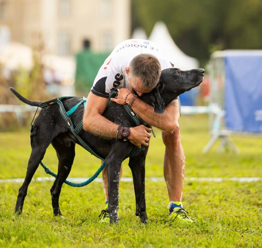 Un maitre et son chien noir se font un câlin durant le Woofest dans un parc après avoir participé à la course.