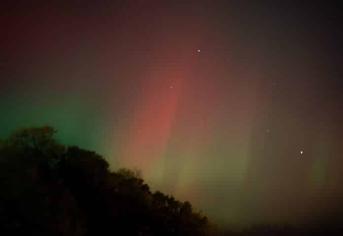 Une aurore boréale rouge et verte dans la nuit au dessus d'une colline.