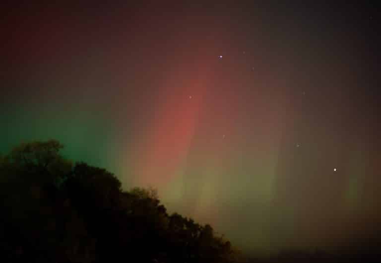 Une aurore boréale rouge et verte dans la nuit au dessus d'une colline.
