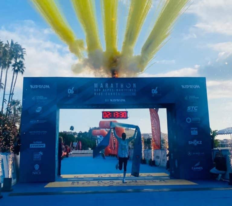 La marathonien Kényan Dickson Kiprop vainqueur de la 17e édiion du marathon Nice-Cannes avec des artifices jaunes au dessus de lui lorsqu'il franchit la ligne d'arrivée en levant les bras.