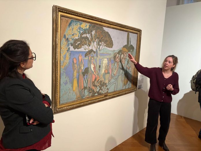 Une femme explique l'histoire d'un tableau de trois quart face durant le vernissage de l'exposition Maurice Denis, Années 1920 l'éclat du midi