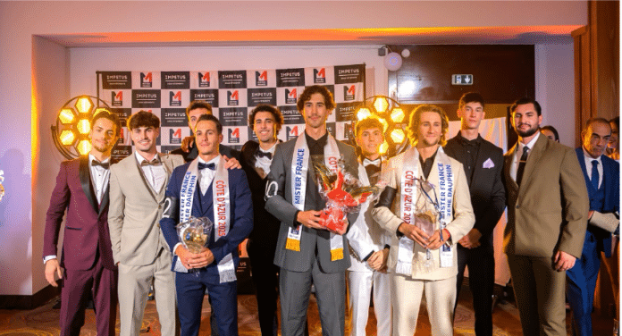 Mister Côte d'Azur France 2025 Mister Côte d'Azur au milieu de ses dauphins du concours. Il est grand les cheveux châtain mi-long en costume gris.