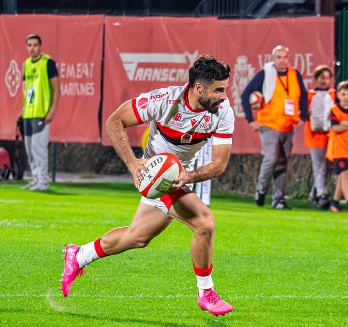Un joueur de Nissa Rugby en maillot blanc rouge et noir avec le ballon s’apprête à faire une passe.