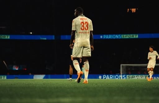 Un joueur de l'OGC Nice, en maillot blanc sur la pelouse du PSG dans un stade plongé dans le noir.