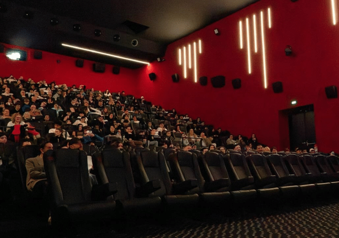 Une salle de cinéma aux murs rouge avec du public.