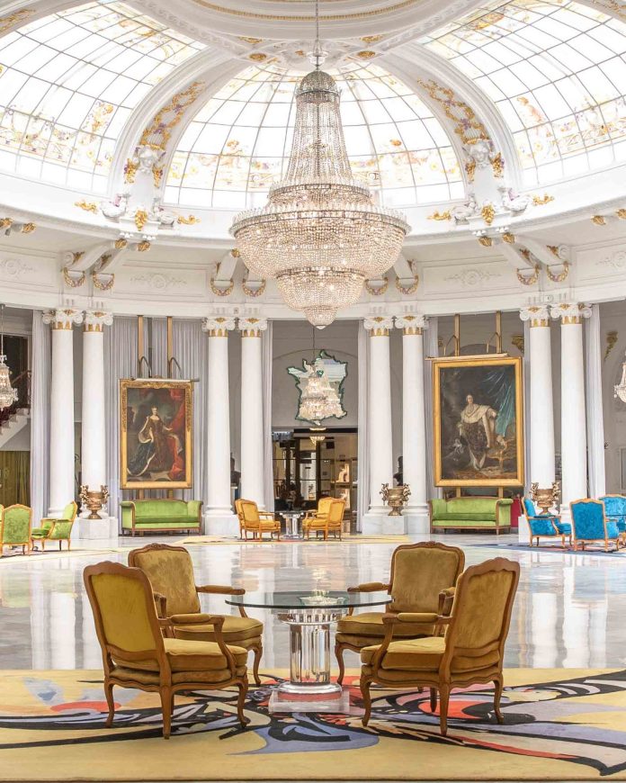 negresco L’intérieur très luxueux du Negresco à Nice avec des table ronde, dans une pièce blanche avec des colonnes, des moulures au plafond et un magnifique lustre au plafond.