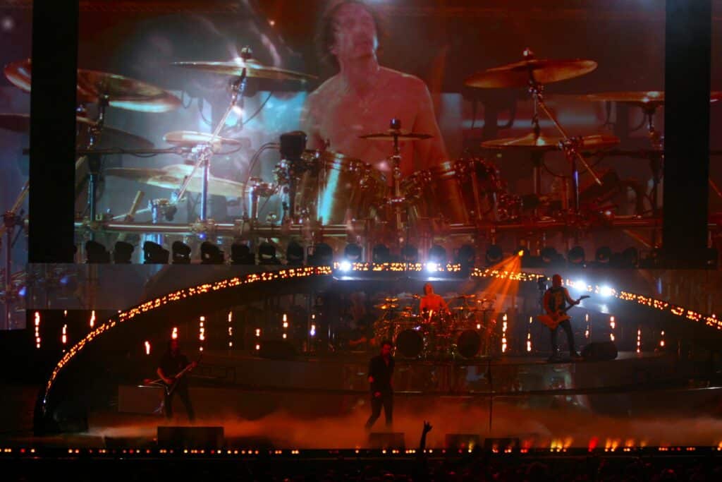 La scène plongée dans le noir avec des touches de rouge et un écran géant qui transmets en image l'image d'un homme transcendé.