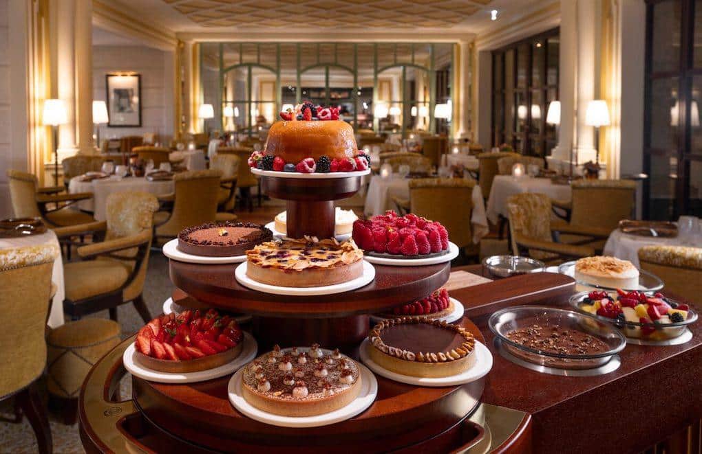 Des gâteaux avec des fruits, du chocolat et différentes formes, tartes, génoise... exposés dans une salle sur un présentoir.