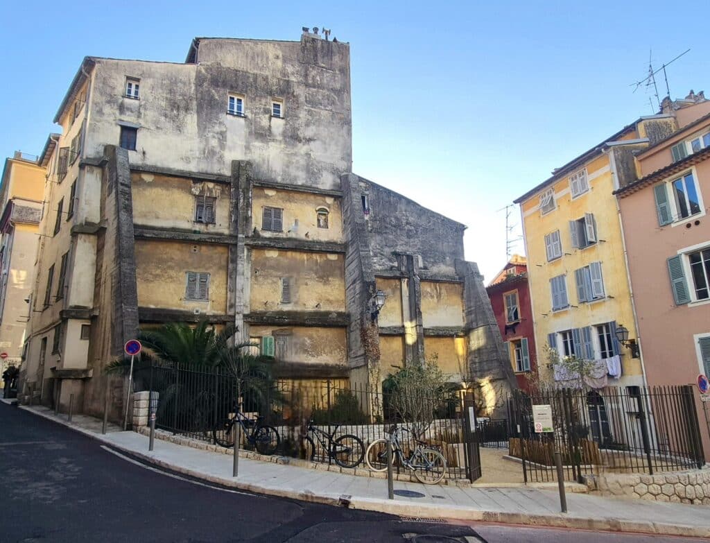 Square Henri Betti dans le centre-ville rénové devenant un petit parc grillagé avec des plantes, des arbres, des bancs en pierre et un trottoir plus grand pour y accéder.