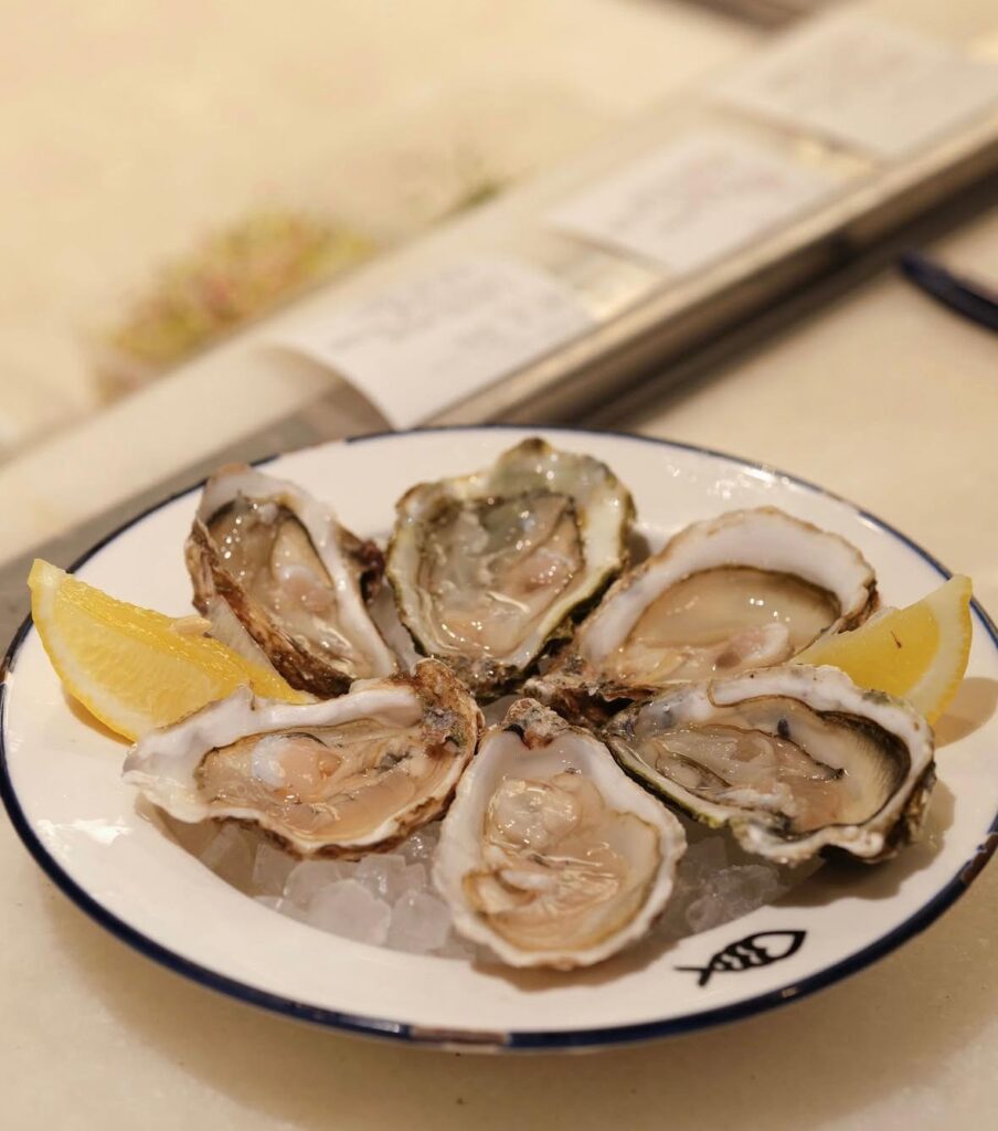 Une assiette d'huîtres du restaurant Peixes avec des tranches de citron.