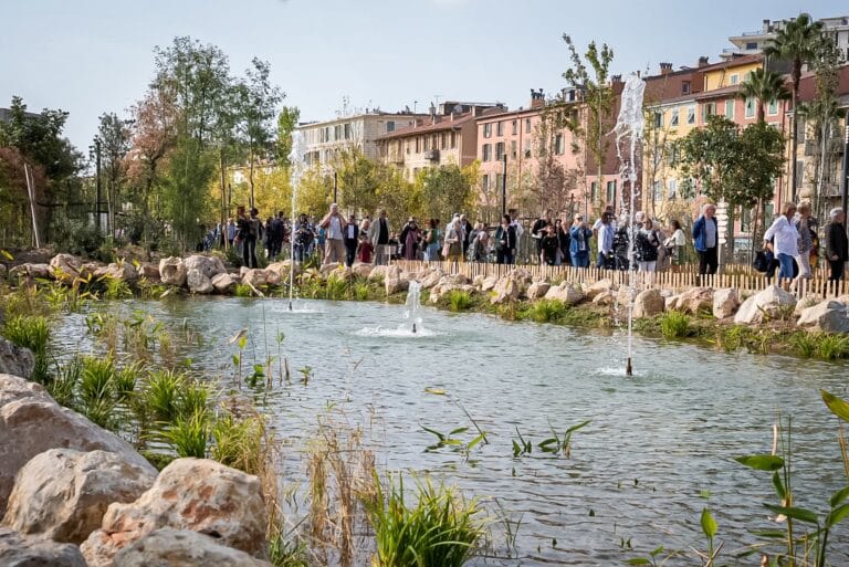 Un petit étang artificiel avec des jets d'eau et de la végétation et des gens qui marche le long de l'eau.