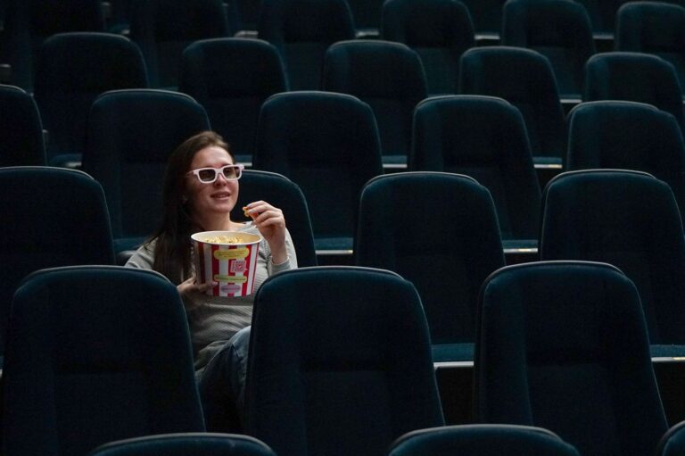 Une personne regarde un film avec des lunettes 3D en mangeant du popcorn dans un siège noir.