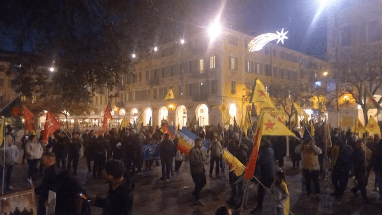Le rassemblement organisé par le PCF06 en soutien au peuple Kurde sur la place Garibaldi de nuit avec une centaine de personnes et des drapeau qui flottent du PCF et en soutien au peuple Kurde.