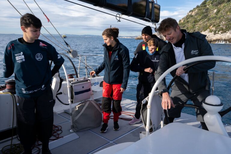 Le navigateur Jean Pierre Dick avec des jeunes sur un bateau de course.
