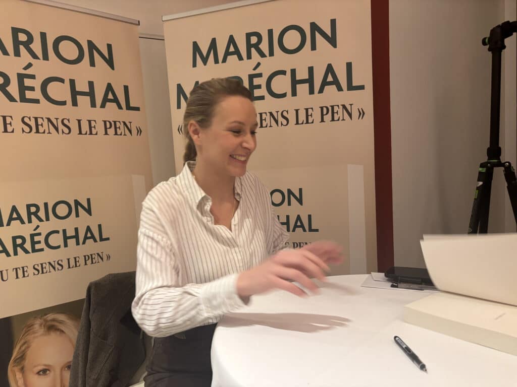 Marion Maréchal en chemise, avec un sourire, pendant sa dédicace.
