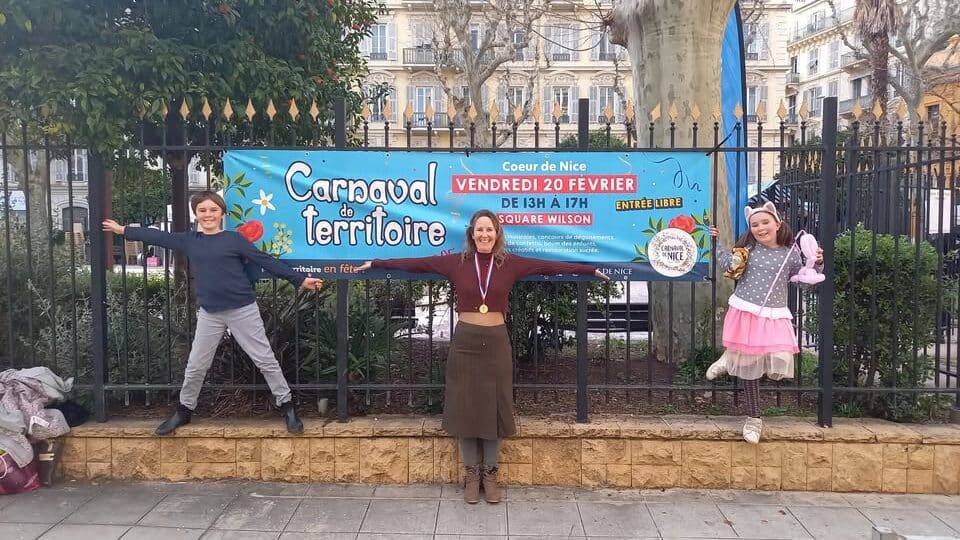la gagnante du battle des mamans médaille autour du coup pose avec ces enfants devant la bannière du carnaval des quartiers