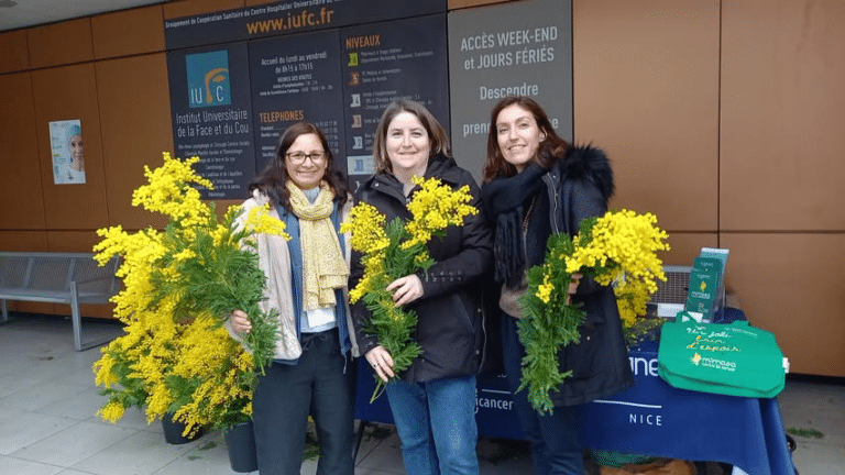 trois femmes avec des bouquets de mimosa à la mains devant l'hopital