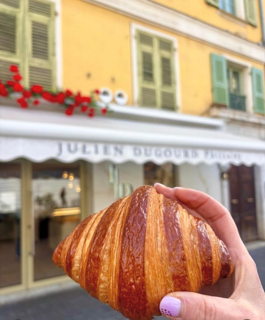 Un croissant tenu dans une main devant la devanture blanche de Julien Dugourd