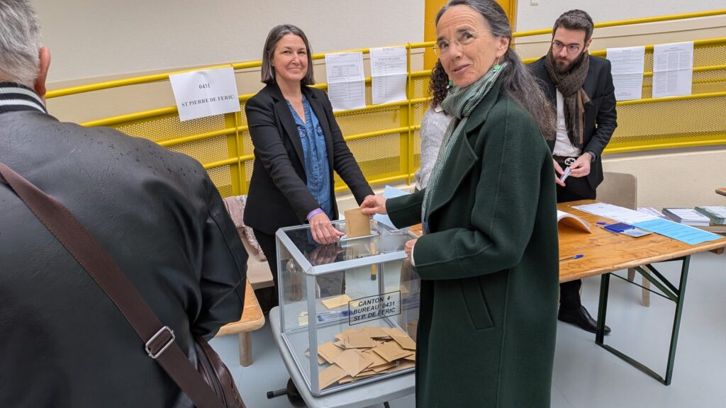 Juliette-Chesnel-Le Roux en manteau vert va déposer son bulletin dans l'urne pour les municipales 2026.