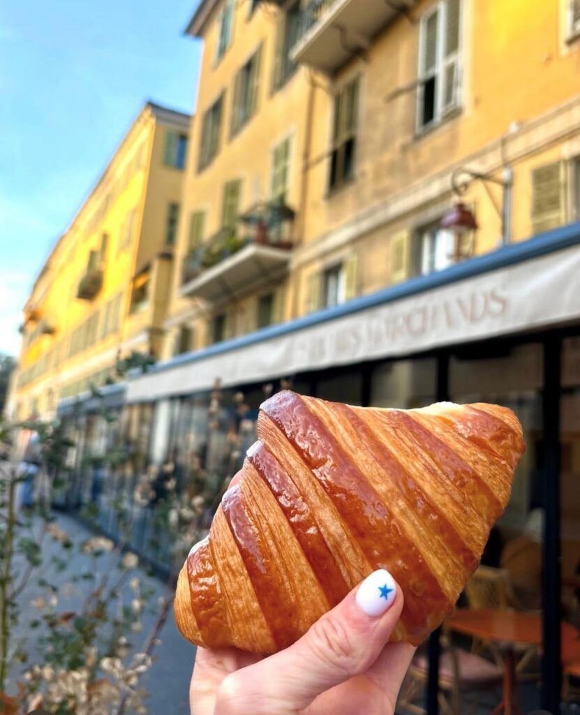Un croissant tenu dans une main devant la devanture des petits marchands.
